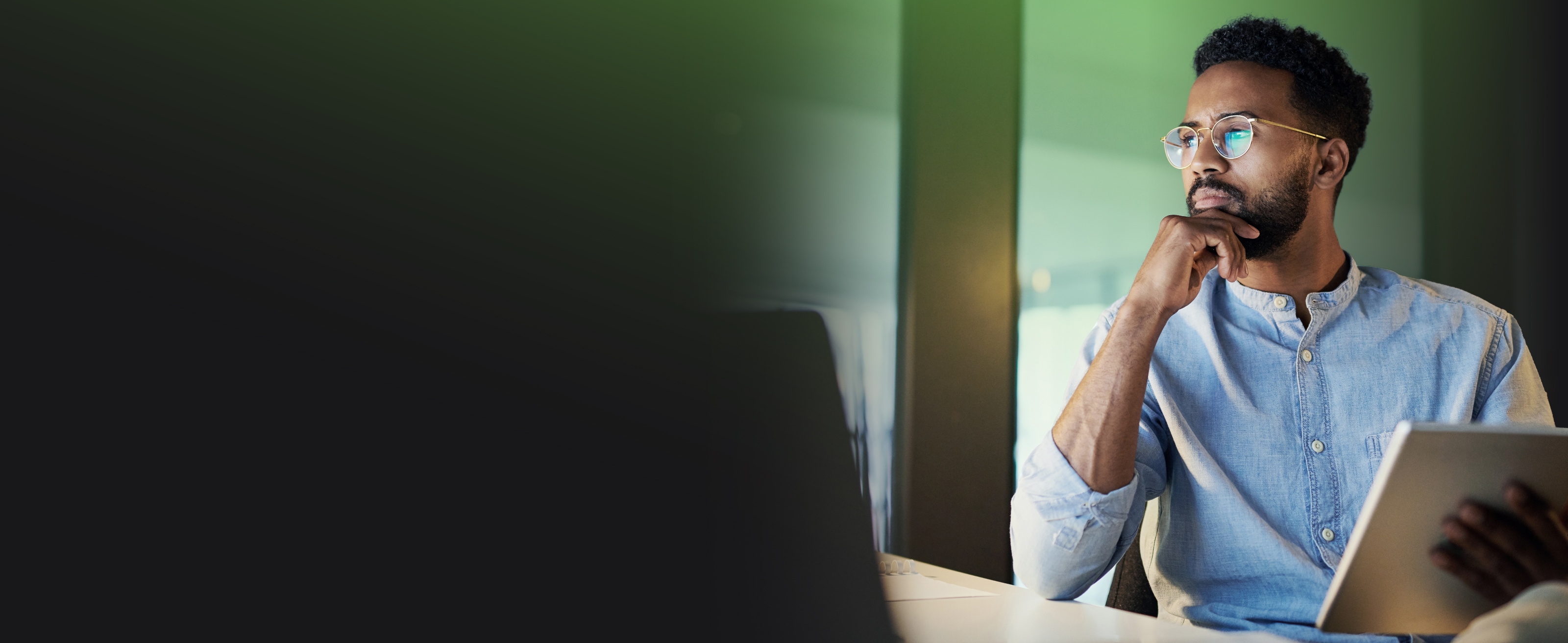 Man in glasses sitting at a desk holding a tablet in his hand