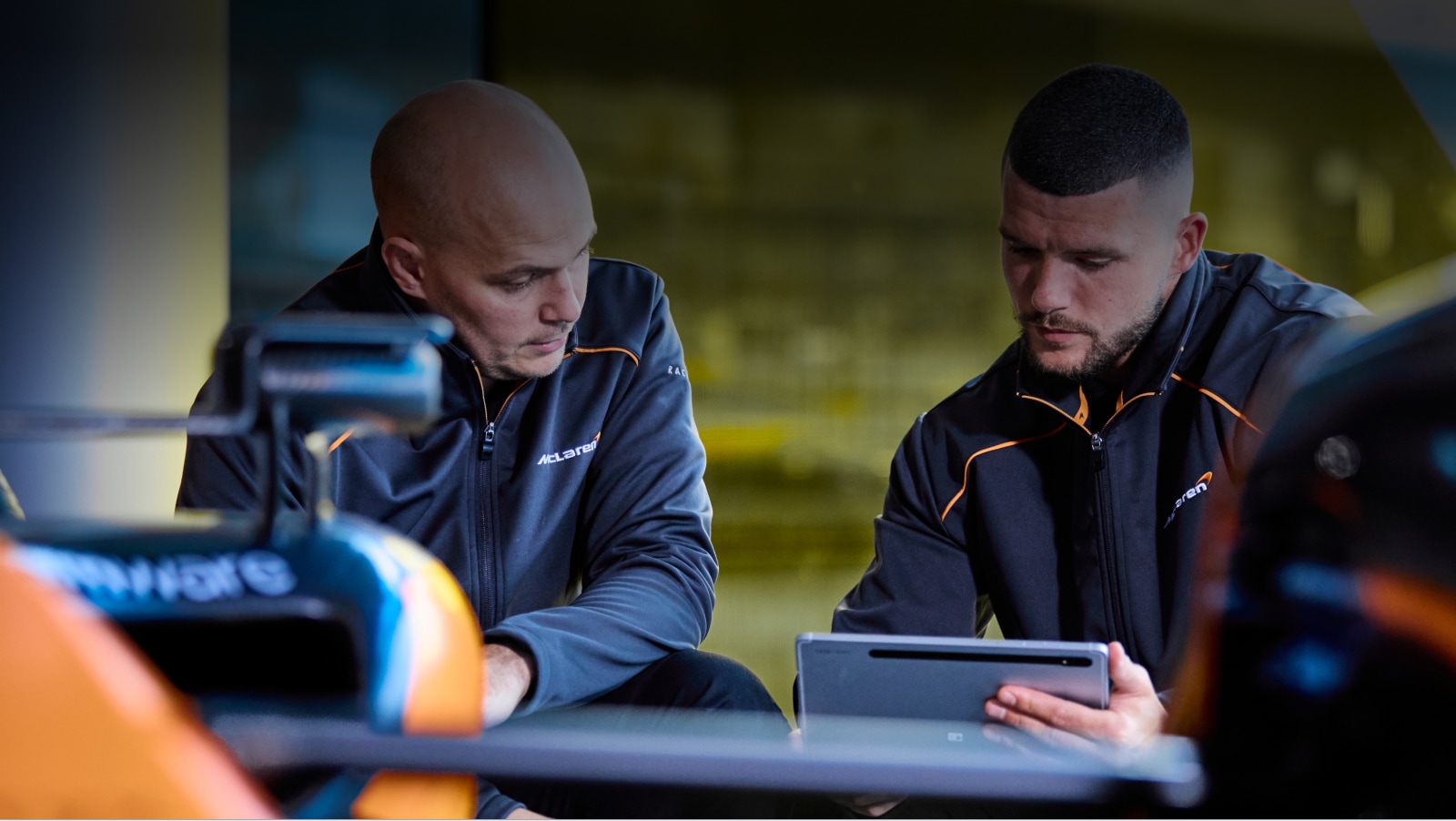 McLaren F1 Team members collaborate on a tablet as they review specs of a McLaren racecar.