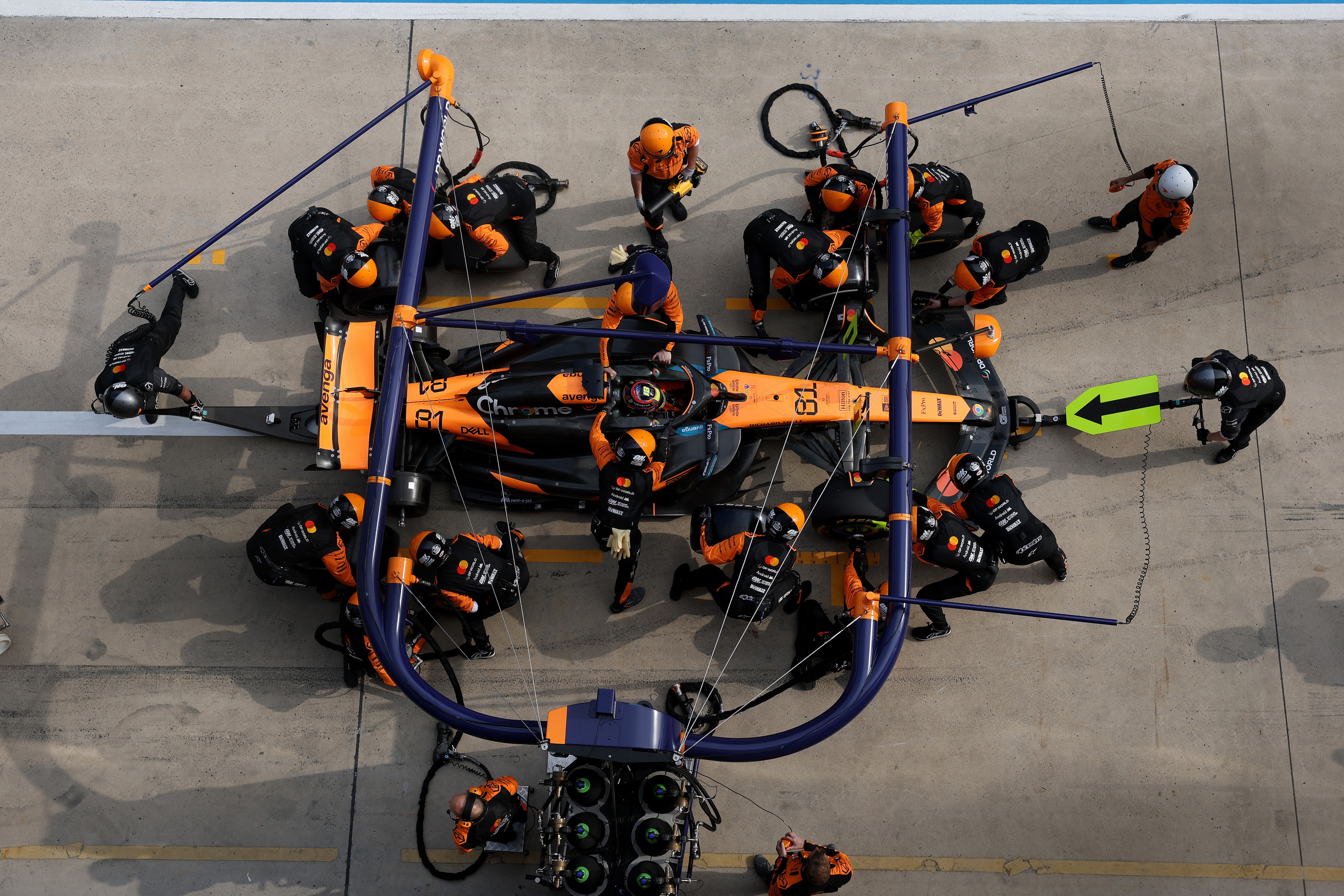 McLaren F1 Team race engineers work on a racecar at a pit stop during a race.