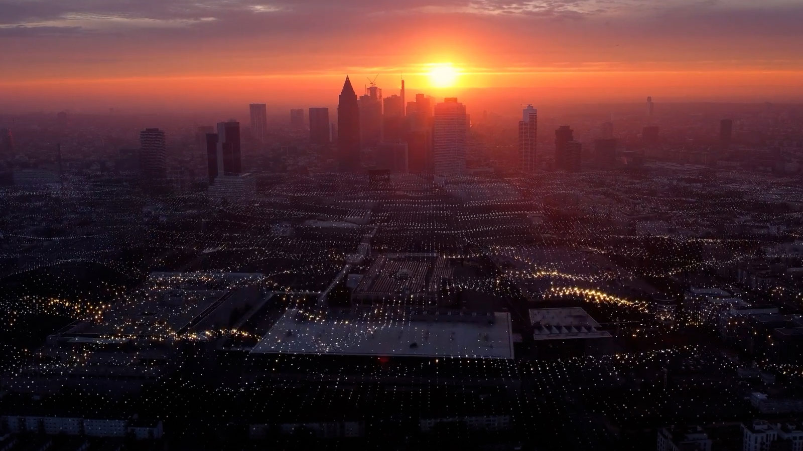 Un coucher de soleil sur la silhouette d’une ville avec un important réseau de lumières au premier plan.