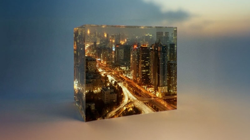 Un cube transparent contenant une ville miniature la nuit avec des gratte-ciel et des autoroutes illuminés.
